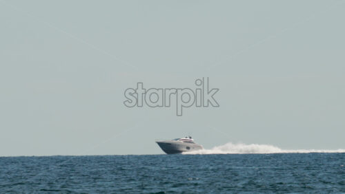 Video - A luxury speedboat racing across open blue water under a clear sky, leaving a long white wake