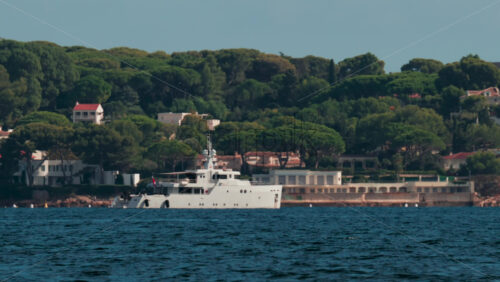 Video - A large white vessel sails along a scenic coastline surrounded by green trees and villas