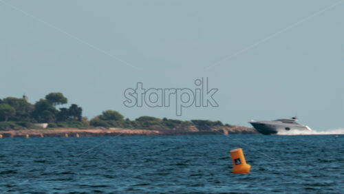 Video - A fast moving yacht glides past a luxury coastal villa surrounded by trees and clear blue water