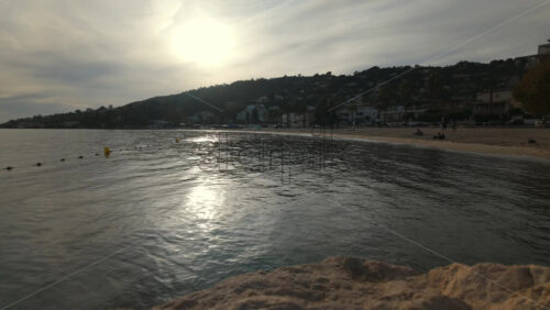 Video - Time lapse of a peaceful seaside view at sunset with gentle waves reflecting golden light and a coastal town in the background