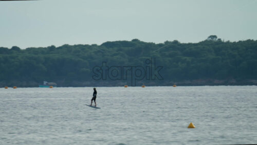 Video - A man balances on an electric foilboard gliding smoothly over the water near the coast