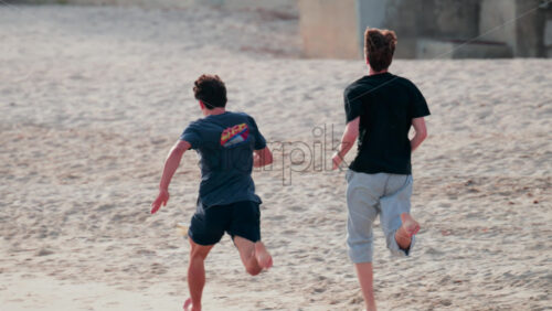 Video - Two young men run barefoot across the sand on a sunny day, enjoying outdoor exercise and friendship