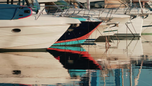 Video - Close up of several yachts moored in a marina, with vivid reflections of their hulls on calm water