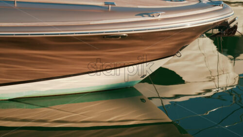 Video - Close up of a yacht's bow shining under warm sunlight, its sleek shape mirrored beautifully on the still green water
