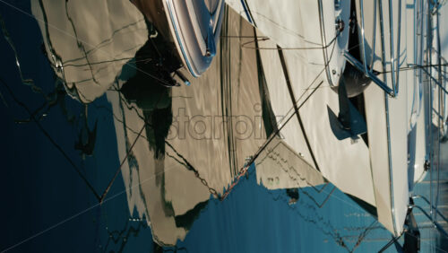 Video - Distorted reflections of yachts, ropes, and anchors on the glossy surface of a marina. Vertical
