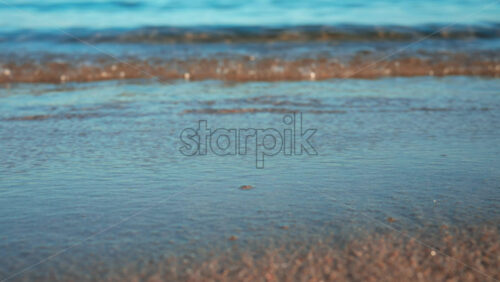 Video - Close up of small waves rolling gently onto the sandy beach under morning light