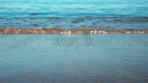 Video - Close up of small waves rolling gently onto the sandy beach under morning light