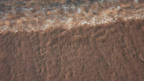 Video - Close up of small waves rolling gently onto the sandy beach under morning light