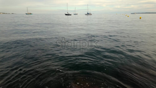 Video - Several sailboats floating peacefully on calm water under a cloudy sky