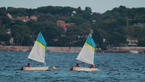 Video - Cannes, France - October 8, 2025: Children in small sailboats learning to navigate on the blue sea near a beach resort