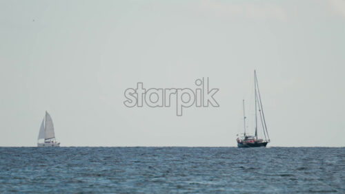 Video - Wide shot of two sailboats navigating the calm blue sea under a pale sky