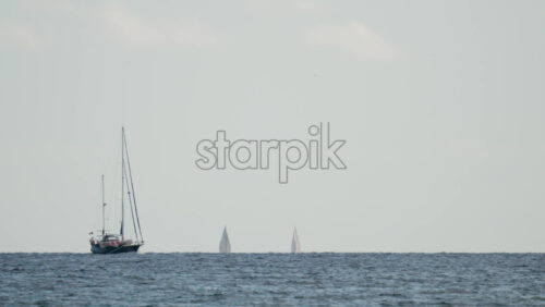 Video - Wide shot of two sailboats navigating the calm blue sea under a pale sky