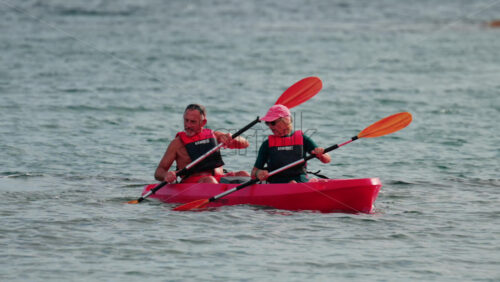 Video - Cannes, France - October 8, 2025: A woman and a man paddling a red kayak on calm blue water wearing a life vest and hat