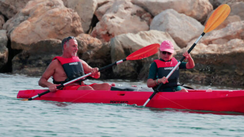 Video - Cannes, France - October 8, 2025: A woman and a man paddling a red kayak on calm blue water wearing a life vest and hat