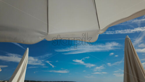 Video - Sunny seaside view with white beach umbrellas framing a bright blue sky and calm sea