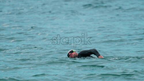 Video - Cannes, France - October 8, 2025: View of a swimmer in wetsuit and cap performing freestyle strokes in open water