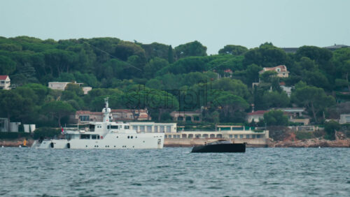 Video - Elegant white yacht anchored off a scenic coastline surrounded by Mediterranean villas and lush pine trees