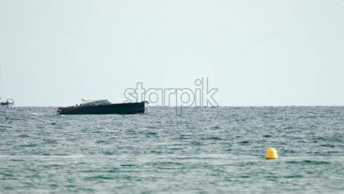 Video - Stylish dark hulled speedboat gliding across the open sea with sailboats on the horizon