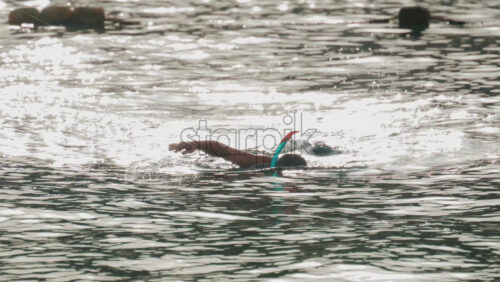 Video - A person swims calmly in the sea with a snorkel, surrounded by sparkling sunlight reflecting off the water's surface