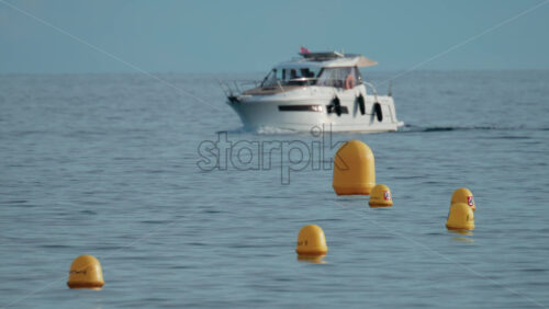 Video - A luxury motor yacht cruises gently across calm blue waters, passing several bright yellow buoys under a clear sky