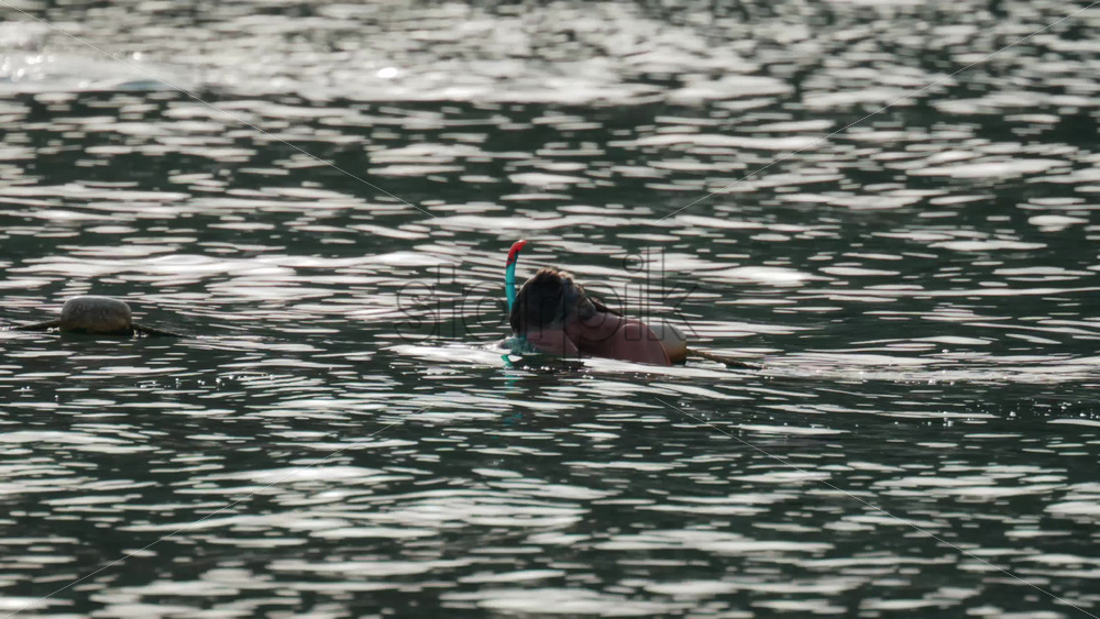 Video - A woman prepares for snorkeling in the ocean, adjusting her mask while floating in gentle water under soft sunlight