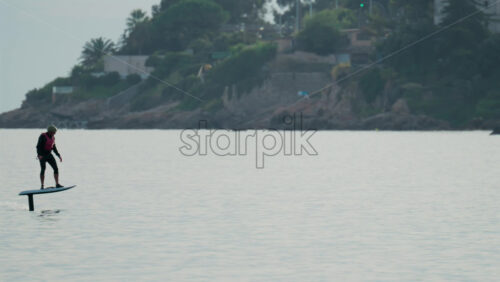 Video - Cannes, France - October 9, 2025: A surfer rides an electric foil board smoothly over the calm Mediterranean Sea near anchored boats