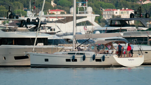 Video - Cannes, France - October 9, 2025: Sailboats and yachts are docked at a marina with people preparing on deck, set against a backdrop of seaside houses and trees