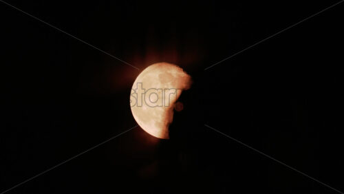 Video - A golden full moon partially covered by drifting clouds in the night sky