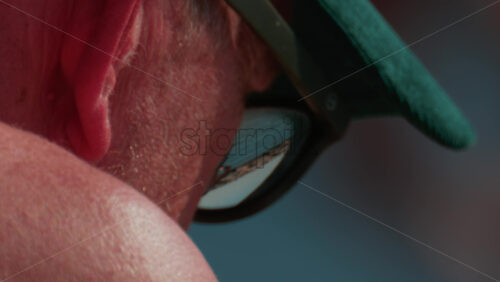 Video - Cannes, France - October 10, 2025: Close up of an elderly man wearing a green cap and sunglasses, sitting by the sea