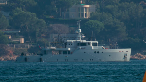 Video - A bright yellow buoy floating on calm blue water with a yacht blurred in the background