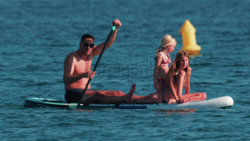 Video - Cannes, France - October 10, 2025: A man paddles on a stand-up board with two young girls enjoying a sunny day at sea