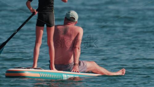 Video - Cannes, France - October 10, 2025: A man sits at the front of a paddleboard while a young child stands and rows at the back