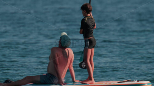 Video - Cannes, France - October 10, 2025: A man sits at the front of a paddleboard while a young child stands and rows at the back