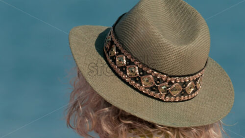 Video - Close up of a decorated sun hat worn by a person facing the calm blue water