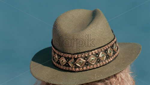 Video - Close up of a decorated sun hat worn by a person facing the calm blue water