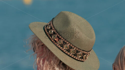 Video - Close up of a decorated sun hat worn by a person facing the calm blue water