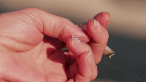 Video - Close up of a relaxed hand holding a cigarette in sunlight by the sea