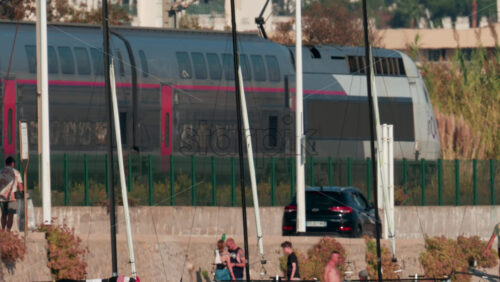 Video - Cannes, France - October 10, 2025: Crowded beach scene with people sunbathing and swimming as a red and black train passes in the background