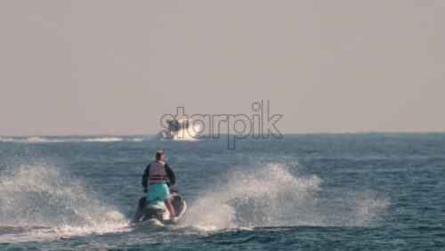 Video - Cannes, France - October 10, 2025: A man on a jet ski speeds across the sparkling blue waters of the French Riviera with a yacht in the background