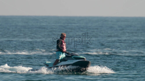 Video - Cannes, France - October 10, 2025: A man on a jet ski speeds across the sparkling blue waters of the French Riviera with a yacht in the background