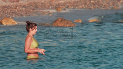 Video - Cannes, France - October 10, 2025: A woman in a green bikini smiles as she enjoys the gentle sea near a rocky beach in Golfe Juan
