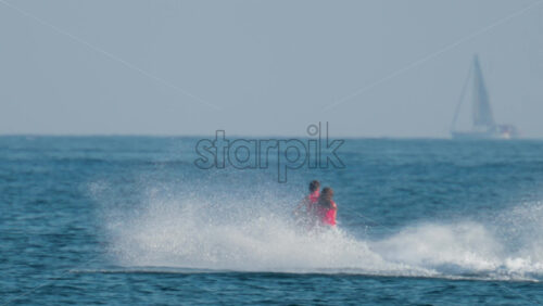 Video - A couple wearing red life vests rides a jet ski across the bright blue sea, splashing water behind them