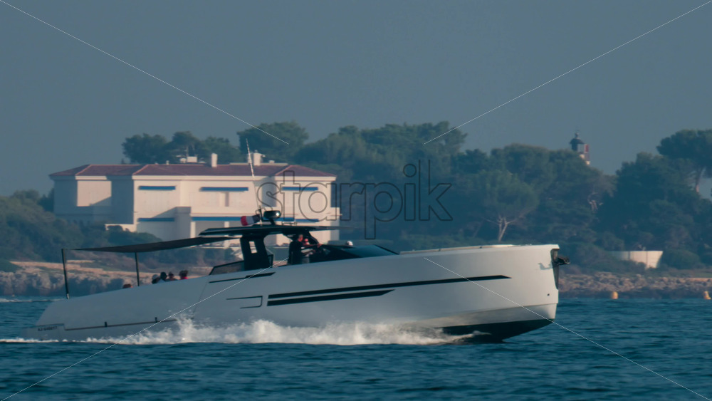 Video - Cannes, France - October 10, 2025: A white sailboat glides near the rocky coastline of the French Riviera, with lush pine trees and elegant seaside villas in the background