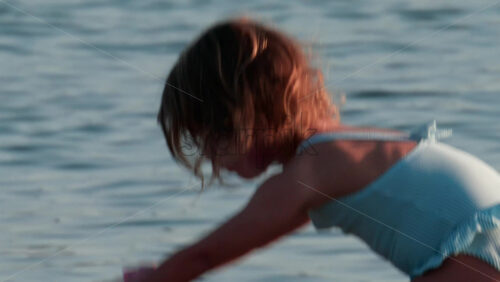 Video - Cannes, France - October 10, 2025: A young girl with golden hair plays by the shore, her face lit by the soft evening sun