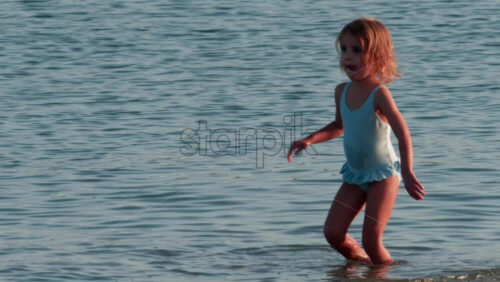 Video - Cannes, France - October 10, 2025: A small child walks slowly through the shallow sea, wearing a light blue swimsuit