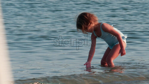 Video - Cannes, France - October 10, 2025: A small child walks slowly through the shallow sea, wearing a light blue swimsuit
