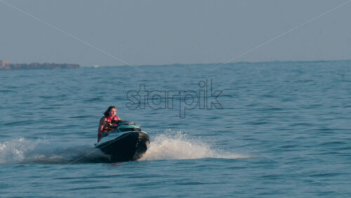 Video - Cannes, France - October 10, 2025: A woman in a red life vest rides a jet ski over gentle blue waves