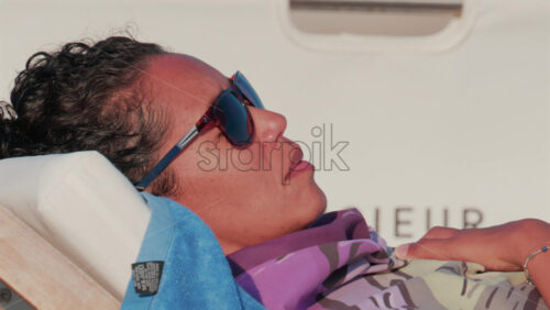 Video - Cannes, France - October 11, 2025: Close up of a woman wearing sunglasses and resting on a towel aboard a yacht