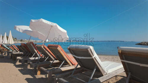 Video - Row of empty sun loungers with white umbrellas on a sandy beach by the calm blue sea