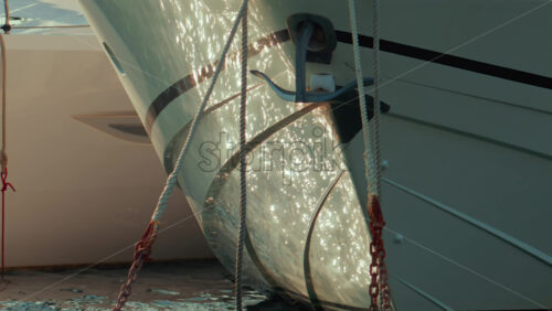 Video - Front view of a yacht's bow with anchor chains and mooring ropes hanging over the sparkling sea